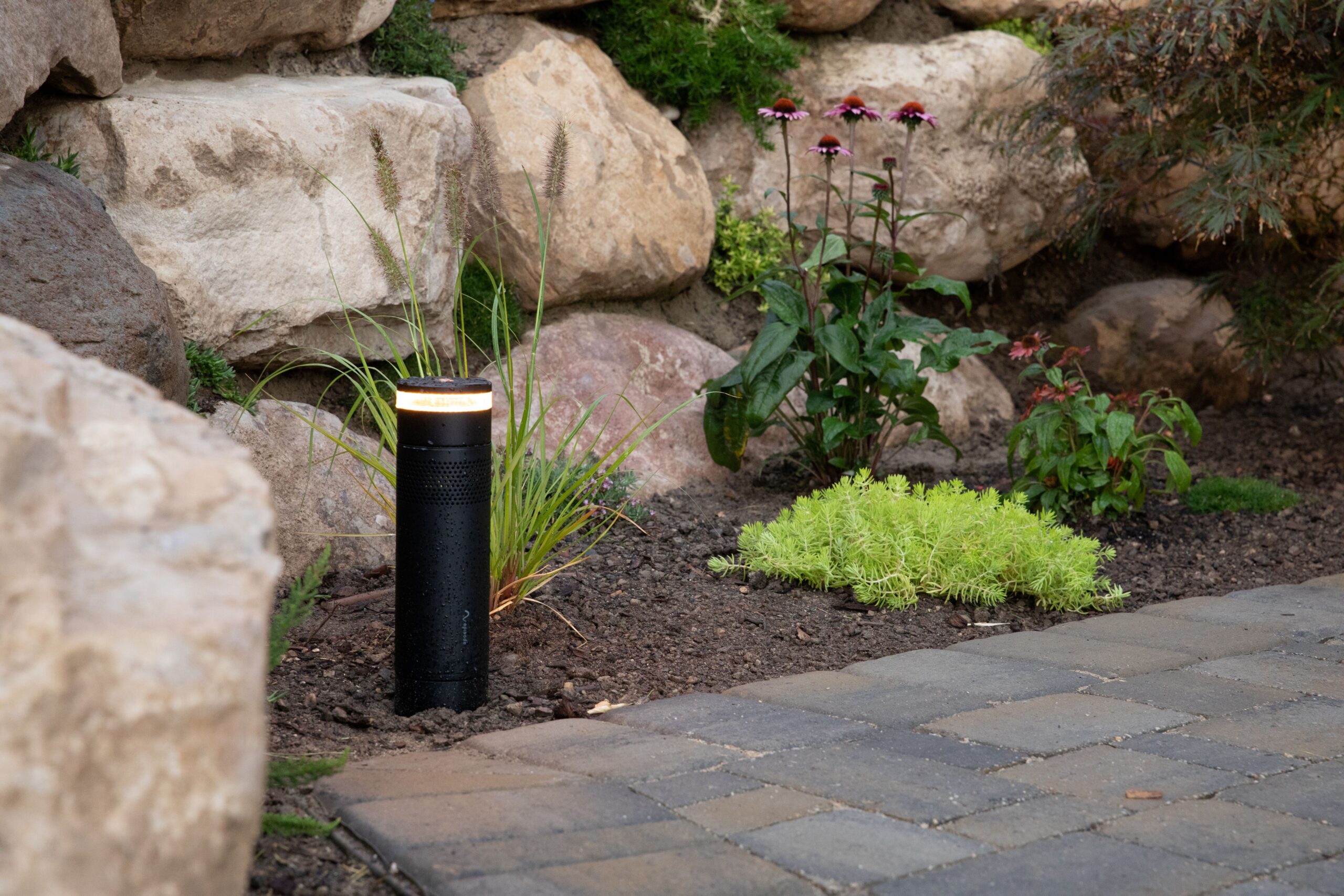 FX Radiance path bollard casting warm light along a paver walk in a landscaped bed
