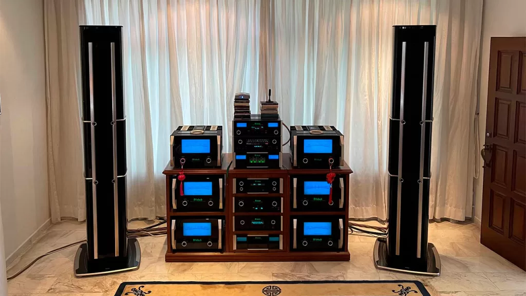 McIntosh amplifiers with blue meters on a wood rack between 2 tall floor speakers