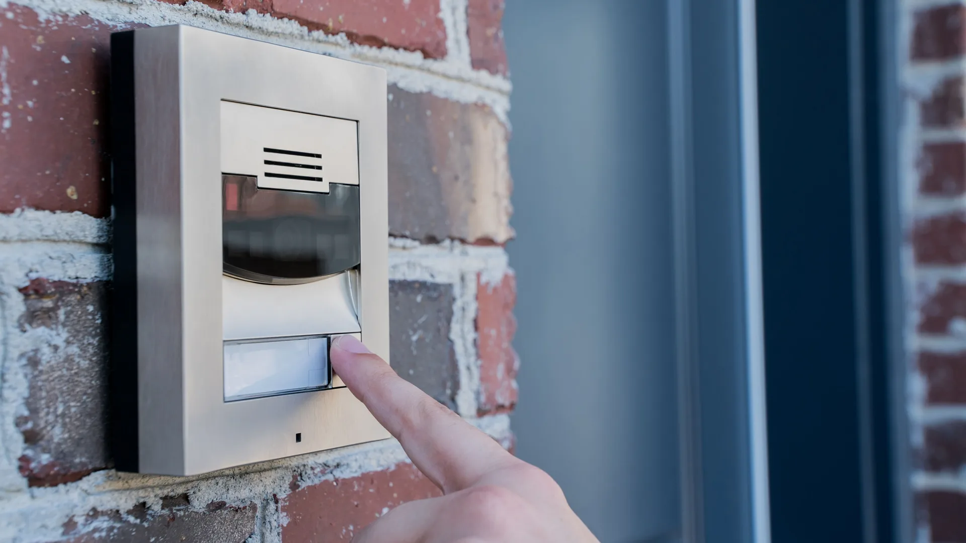 Finger pressing a doorbell button on a brick wall by a front door in Northern New Jersey